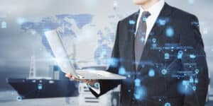 European businessman using laptop with abstract glowing blurry global delivery scheme hologram on transport dock background.